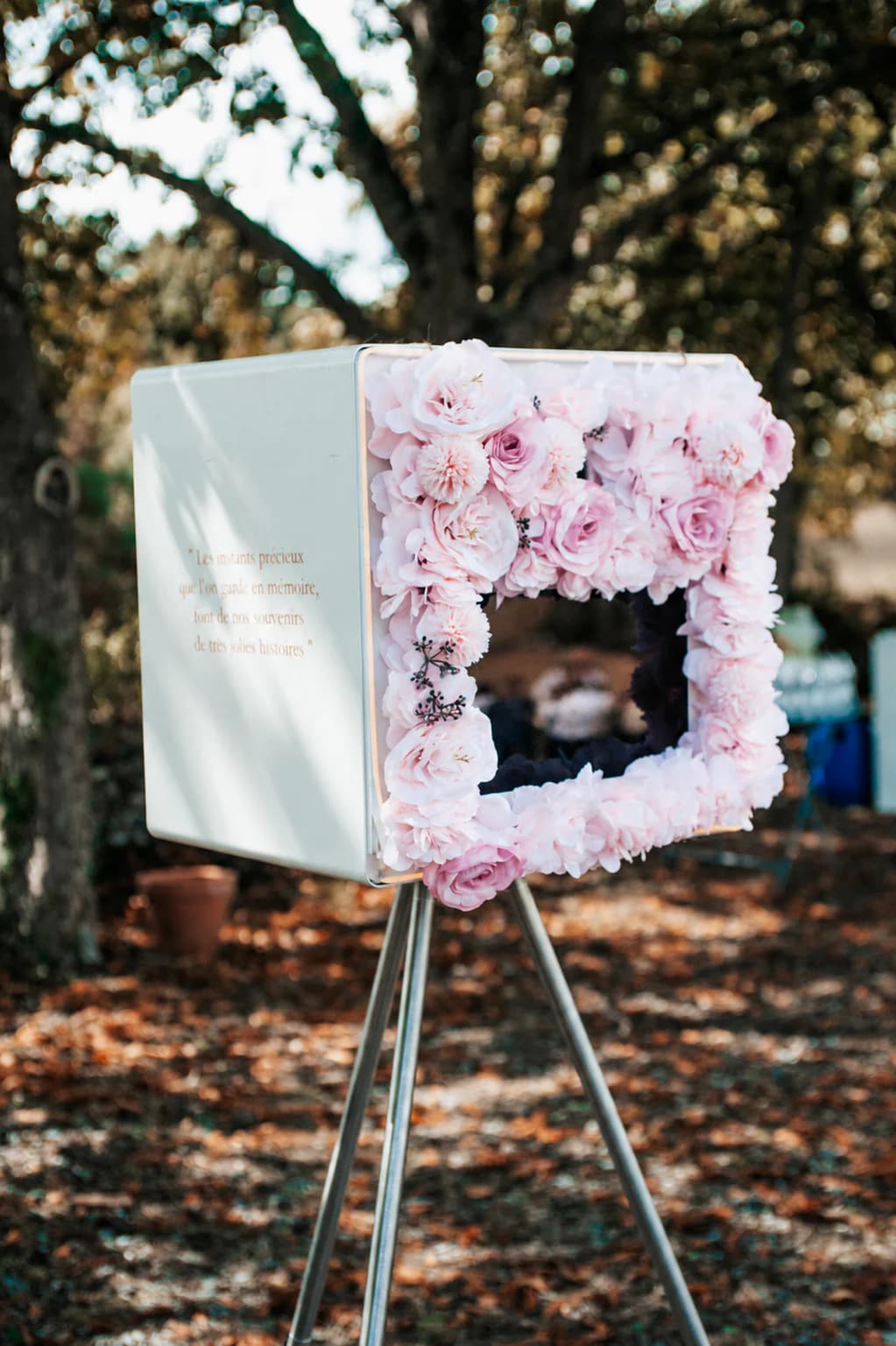 Photobooth ivoire orné de fleurs roses sur son trépied dans un décor boisé